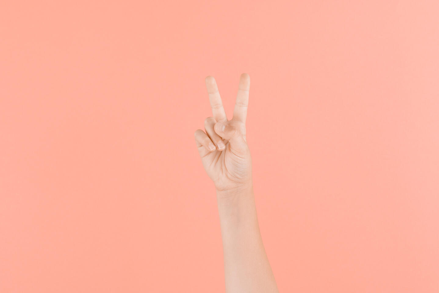 Kids hand two fingers raised pink background